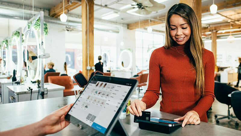 A woman in a red sweater swiping a credit card to pay at a check out counter.