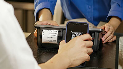 A woman in a red sweater swiping a credit card to pay at a check out counter.